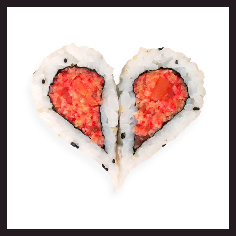 Rouleau de sushi coupé et arrangé pour former un cœur, rempli d'ingrédients rouges et orange, sur fond blanc.