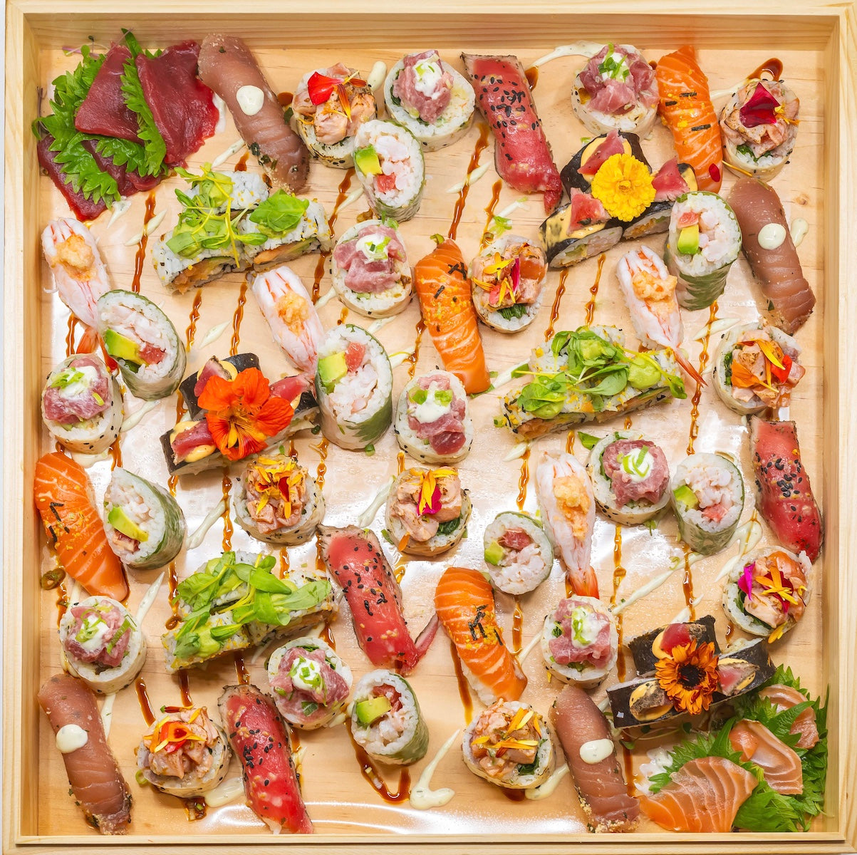 Un plateau en bois rempli de rouleaux de sushi, de sashimi, de nigiri et de garnitures assortis, disposés de manière organisée et colorée.