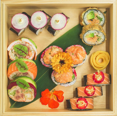 Un plateau en bois contenant une variété de sushis et de sashimis, garni de micropousses, d'une tranche d'agrumes et de pétales de fleurs comestibles.